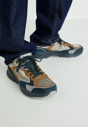 Des baskets multicolores avec un mélange de matériaux en daim et en maille, ornées d'accents gris, marron et vert, ainsi qu'une semelle texturée.