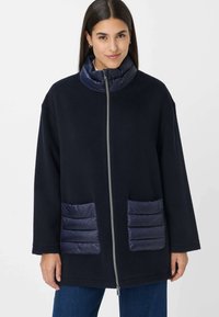 Giacca in pile blu navy con tasche e colletto imbottiti e trapuntati. Presenta una cerniera frontale e vestibilità rilassata. Tessuto strutturato con accenti lisci.