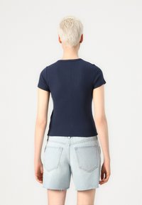 Haut à manches courtes à côtes navy associé à un short en denim clair. Le haut présente un col rond et une silhouette ajustée.