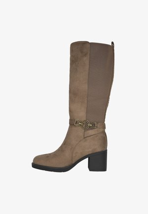 Bota marrón hasta la rodilla con un material similar al ante, un panel texturizado y un acento de cadena metálica cerca del tobillo. Tacón grueso para mayor estabilidad.