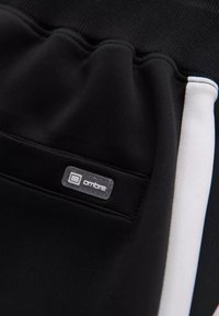 Zwarte sweats met een gladde textuur, een witte accentstreep en een klein doorzichtig label met "ombre" op de zijkant van de zak.