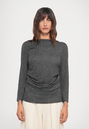 Gray long-sleeve top with draped detailing at the front, round neckline, and soft texture, paired with light-colored pleated pants.