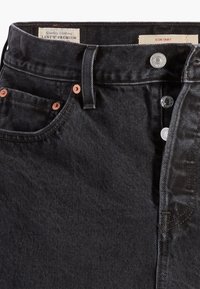 Jupe en denim noir Levi's avec rivets en cuivre, fermeture à boutons visible, passants de ceinture et étiquettes indiquant Levi's Premium et Icon Skirt.