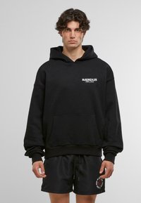 Černá mikina s kapucí vyrobená z měkké látky, se klokánkovou kapsou, s bílým logo textem na prsou a žebrovanými manžetami a lemem.