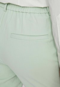 Pantalons verts clairs à taille élastique avec une poche arrière et un détail de couture subtil. Le matériau a une finition lisse et texturée.