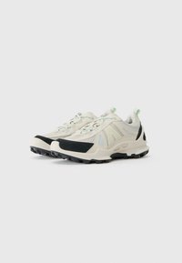 Sport Sneakers mit einem beigen Obermaterial und schwarzen Akzenten, strukturiertem Mesh, reflektierenden Details und einer robusten Gummisohle mit einem gemusterten Profil.