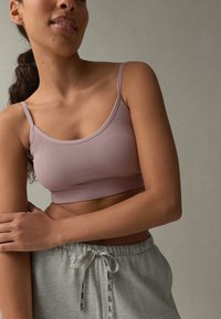 Bralette viola chiaro a coste con spalline sottili, abbinato a pantaloni della tuta grigi con coulisse e fascia con logo intorno alla vita.
