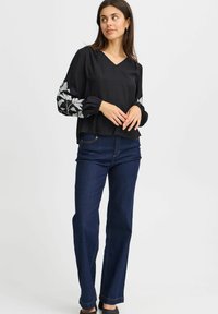 Blusa nera con scollo a V e maniche a sbuffo elastiche, impreziosita da ricami di foglie d'argento. Abbinata a jeans dritti blu scuro.