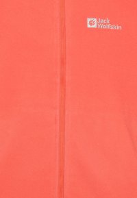 Veste en polaire corail avec fermeture éclair complète, présentant un petit logo blanc sur le côté gauche. Texture lisse et tissu doux.