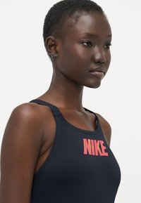 Črn športni top s tankimi naramnicami. Ima izstopajoč roza Nike logotip na prsih. Gladka tekstura, prilegajoč dizajn.