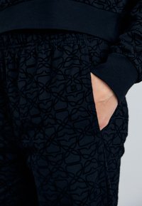 Joggers neri con motivo, caratterizzati da un design testurizzato, dotati di una vita elastica e tasche laterali. Il materiale sembra morbido e flessibile.