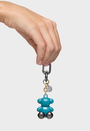 Hand holding a black clasp keyring with a small teal bear-shaped charm and a silver round tag attached.
