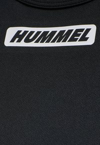 Black athletic shirt featuring a textured fabric with a white rectangular label displaying the word "HUMMEL" in a bold, stylized font.