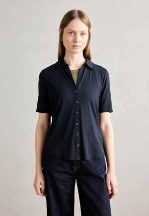 Marine blouse met kraag, korte mouwen en een gladde textuur, gecombineerd met blauwe jeans. Heeft bruine knopen en een subtiele glans.