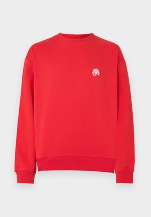 Sweat-shirt rouge à manches longues avec col ras du cou et petit trèfle à quatre feuilles blanc brodé sur la poitrine gauche.