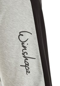 Sive in črne trenirke z mehko teksturo, ki vključujejo napis "Winshape" na sivi sekciji. Minimalistična zasnova in kontrastne barve.