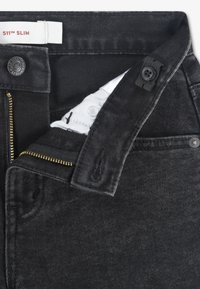 Μαύρο τζιν 511 Slim από τζιν υλικό με φερμουάρ χρυσού χρώματος, εσωτερική λεπτομέρεια υφάσματος και λευκή ετικέτα με κόκκινο κείμενο.