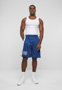Navy atletik shorts med hvid sidepanel og broderet nummer "89." Bæret med en hvid tanktop og hvide sneakers. Ensfarvet baggrund.