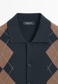 Cardigan lavorato a maglia in blu navy e marrone con motivo a diamante, dotato di collo con risvolto, chiusura frontale con bottoni e cuciture bianche a contrasto.