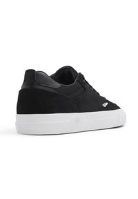 Svart semsket sneakers med et teksturert stoffoverdel, kontrasterende lærdetaljer og en hvit gummisåle. Har en logo nær hælen.