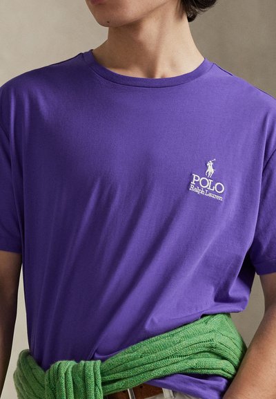 T-shirt en coton violet à manches courtes, avec un petit logo blanc "Polo Ralph Lauren" et une ceinture tricotée verte autour de la taille.