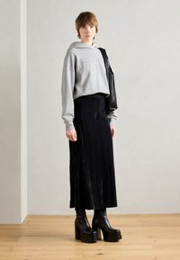 Grå kort hoodie med preget logo, svart plissé maxi skjørt og chunky svarte plattformstøvler. Jevn tekstur, avslappet passform og lagdelt utseende.