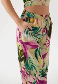 Pantaloni stampati floreali di colore giallo chiaro con foglie tropicali verdi e rosa. Presentano una vita elastica e tasche laterali. Tessuto morbido e leggero.
