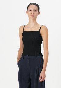 Black ribbed tank top with square neckline and thin straps, paired with navy high-waisted trousers. Smooth texture and fitted design.