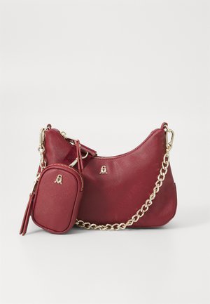 Sac à main en cuir texturé rouge avec une petite pochette détachable, une bandoulière en chaîne dorée et des embellissements en logo doré sur fond blanc uni.