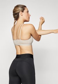 Sostén deportivo de color beige claro con tirantes dobles ajustables y diseño ajustado, combinado con leggings negros de cintura alta que presentan una cinturilla texturizada.