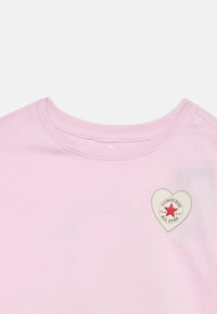 Ανοιχτό ροζ κοντομάνικο με στρογγυλή λαιμόκοψη, με λευκή καρδιά σε σχήμα λογότυπο Converse All Star που φέρει κόκκινο αστέρι στο στήθος.