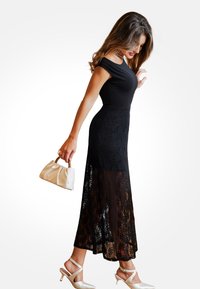 Černé šaty s krátkými rukávy a krajkovou aplikací, s těsným živůtkem a rozšířenou sukní. Doplněné bílou kabelkou a světlými botami.