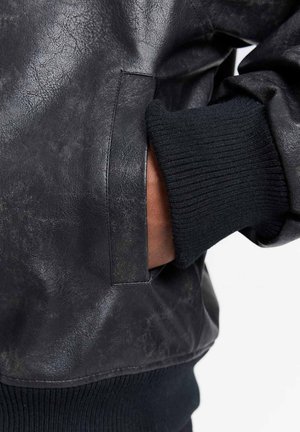 Giubbotto in pelle nera con polsini a coste neri. Il tessuto presenta una finitura testurizzata ed ha un dettaglio di tasca laterale sulla vita.