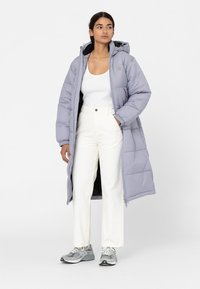Licht paarse gewatteerde lange jas met capuchon, voorzien van een ritssluiting, zijzakken en elastische manchetten, gecombineerd met witte broek en grijze sneakers.