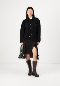 Schwarze Jeansjacke, schwarzer, geraffter Rock, braune knielange Stiefel mit Schnallen und eine kleine schwarze Handtasche. Glatte Texturen und modernes Design.