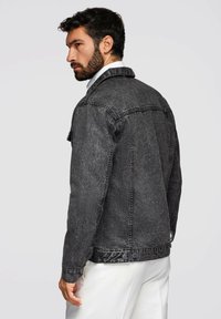 Giacca in denim grigia da uomo con colletto classico, chiusura a bottoni e due tasche laterali. Tessuto strutturato con un look leggermente usurato.