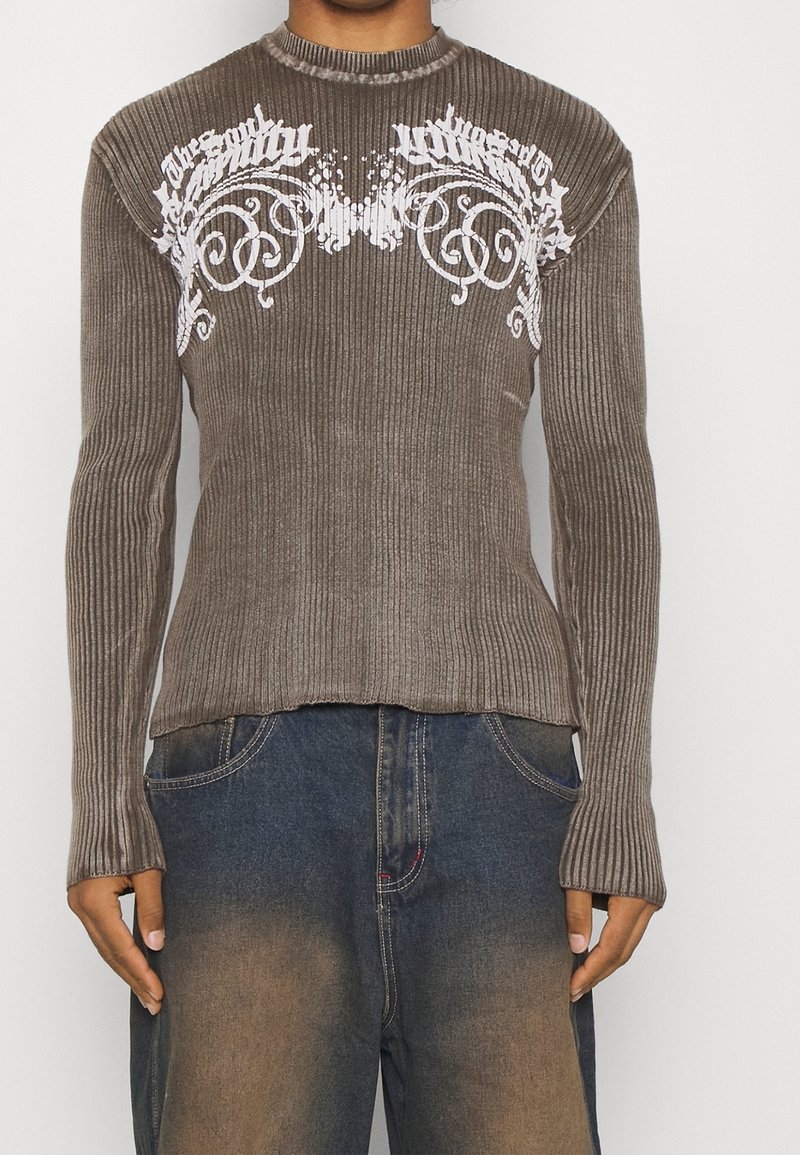 Brown ribbed long-sleeve top featuring white graphic text and swirling designs across the chest, with a high neckline and fitted silhouette.