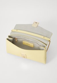 Borsa a mano in pelle gialla con una texture liscia, hardware dorato e una tracolla a catena. L'interno presenta un rivestimento in suede beige e una tasca con zip.