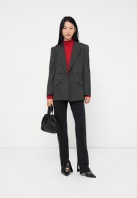 Double-breasted gray pinstripe blazer over a red turtleneck, paired with black jeans and a small black bag. Pointed black heels accent the outfit.
