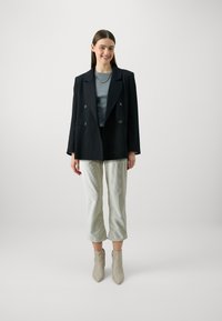 Black double-breasted blazer over a gray top, paired with light green cropped pants and beige ankle boots. Simple, clean design.