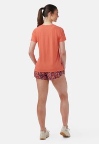 Orange kortärmad skjorta med raglanärmar, i kombination med mönstrade shorts i blått, rött och vitt. Sneakers i beige färg med strukturerade sulor.