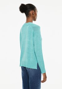 Turquoise sweater with a textured finish, ribbed trim, and a slightly oversized fit. Features a rounded neckline and side slits.