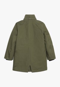 Płaszcz oliwkowozielony o prostej, gładkiej fakturze, z rozporkiem z tyłu i minimalistycznym designem. Bez widocznych metalowych elementów ani ozdób.