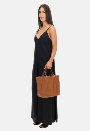 Borsa tote in pelle marrone con manici intrecciati, hardware in argento e dettagli di cucitura. Il modello indossa un maxi abito senza maniche nero.