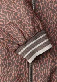 Manica di giacca con stampa leopardata e polsino a costine con strisce beige e bianche, e una cerniera metallica visibile su tessuto stampato.