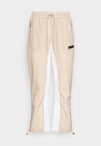 Beige och vita färgblockerade byxor med dragsko i midjan, dragkedjefickor och justerbara benslut med snöra. Lättviktigt tyg.