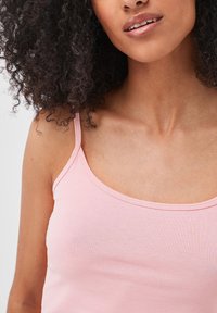 Débardeur rose clair avec des bretelles réglables, en tissu doux et décolleté en ronde. Texture lisse avec des détails de couture minimaux.