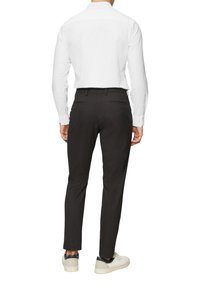 Chemise habillée blanche pour homme avec des manches longues, associée à un pantalon noir et des chaussures blanches. Présente un col classique et une coupe ajustée.