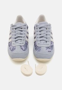 Light blue athletic shoes with suede and snake print accents, featuring three white stripes, round laces, and a textured rubber sole.
