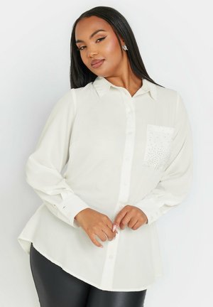 White long-sleeve shirt with a button-down collar, curved hem, and a pocket adorned with small rhinestones for decoration. Smooth fabric texture.